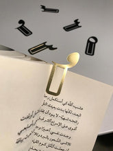 Load image into Gallery viewer, Arabic brass metal bookmark in the shape of damma diacritic used in an arabic book