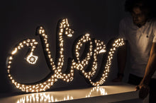 Load image into Gallery viewer, A 1m long ramadan decoration, 3D free standing sign light of the term &quot;Ramadan&quot; in Arabic calligraphy. Metal front with arabic letters cutout placed on a table next to a male model
